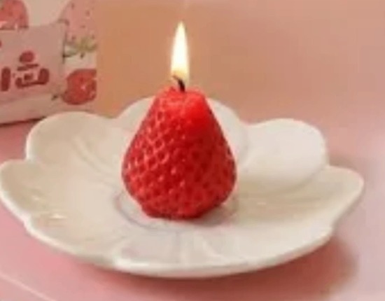 A single strawberry beeswax candle burning on a small flower dish