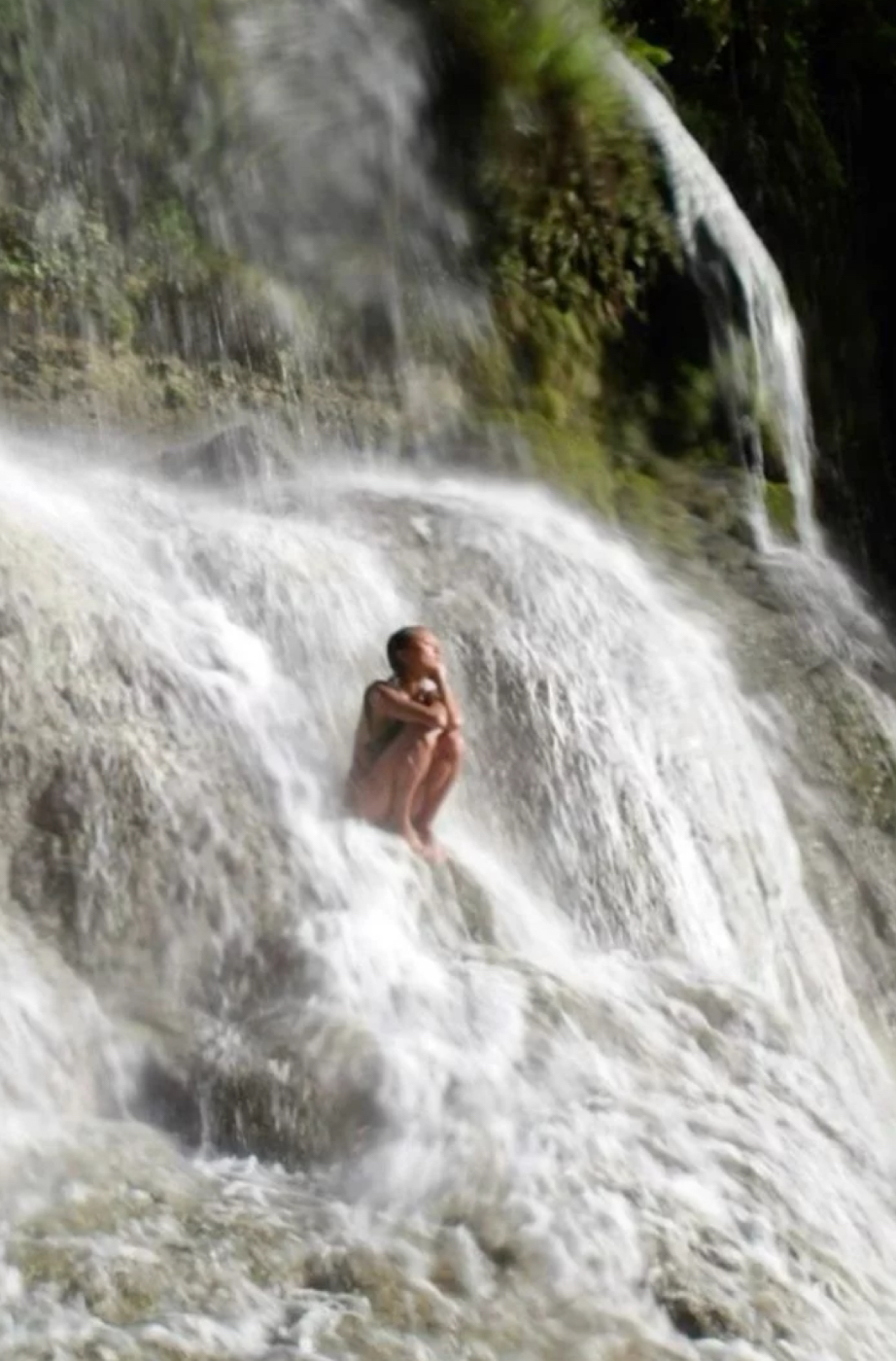 Woman held in a waterfall, letting the moving water carry her into stillness